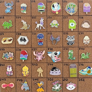 May include: A collection of enamel pins featuring various cartoon characters and designs. The pins include characters like Stitch, Buzz Lightyear, and Marie, along with other themed items such as ice cream bars and coffee cups. The pins are displayed on a corkboard.