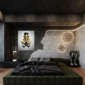 May include: A black and gold 3D sculpture of a cartoon character wearing a top hat and holding a skull and crossbones. The sculpture is hanging on a white wall in a modern bedroom with a black bed and green headboard. The room has a concrete wall with a decorative light fixture.