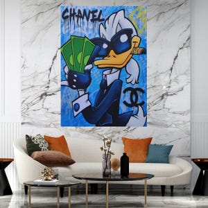 Può includere: Un'anatra di cartone animato con occhiali da sole e un vestito tiene un mucchio di soldi e un sigaro. Lo sfondo è blu con la parola "CHANEL" in vernice che cola e il logo Chanel.