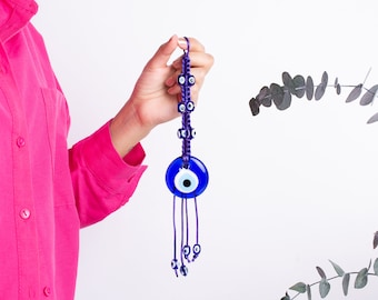 May include: A blue and purple evil eye charm with a beaded tassel. The charm is made of glass and has a blue eye with a white pupil. The tassel is made of purple string and has small blue beads.