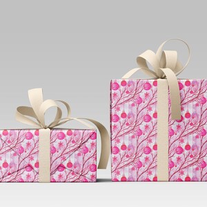 May include: Two wrapped gift boxes with a festive Christmas design. The wrapping paper features a pattern of pink ornaments, branches, and snowflakes on a white background. Each box is tied with a cream-colored ribbon.