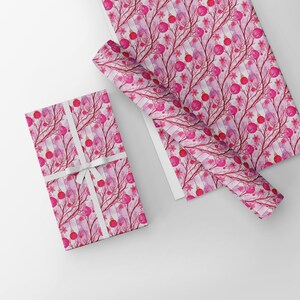 May include: Gift-wrapped box and wrapping paper featuring a watercolor design of pink orbs, branches, and floral accents on a white background. The box is tied with a white ribbon. The paper is rolled and flat.