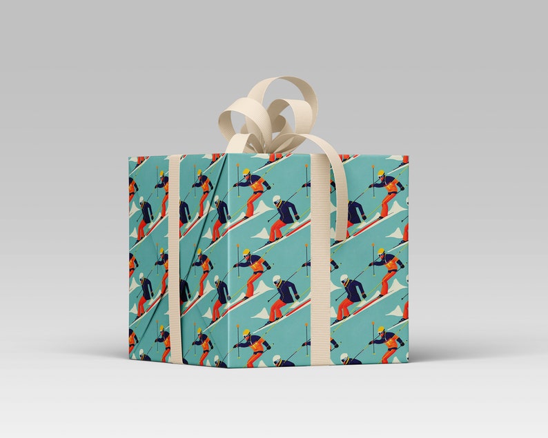 May include: A wrapped gift box featuring a repeating pattern of skiers on a light blue background. The skiers are depicted in a retro style, wearing orange and blue ski suits. The box is tied with a cream-colored ribbon and bow.