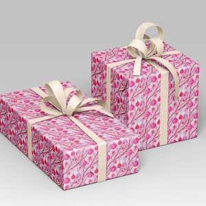 May include: Two gift boxes wrapped in pink patterned paper with a cream-colored ribbon and bow. The paper features a watercolor design of pink berries and branches on a white background. The boxes are rectangular.