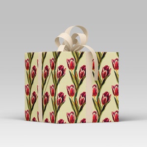 May include: A square gift box wrapped in paper with a repeating pattern of red tulips on a cream background. The box is tied with a cream-colored ribbon and bow, creating a classic and elegant presentation.
