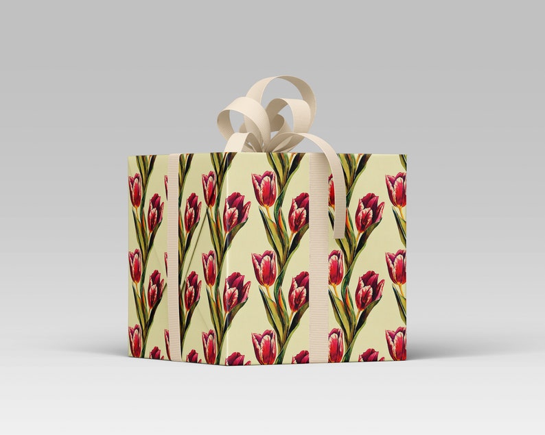 May include: A square gift box wrapped in paper with a repeating pattern of red tulips on a cream background. The box is tied with a cream-colored ribbon and bow, creating a classic and elegant presentation.