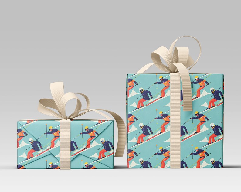 May include: Two gift boxes wrapped in light blue paper with a repeating pattern of skiers on a snowy mountain. The skiers wear orange and blue outfits. The boxes are tied with cream-colored ribbon.