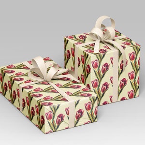 May include: Two gift boxes wrapped in floral patterned paper featuring red tulips on a cream background. Each box is tied with a cream-colored ribbon and bow, creating a classic and elegant presentation. The boxes are ideal for special occasions.