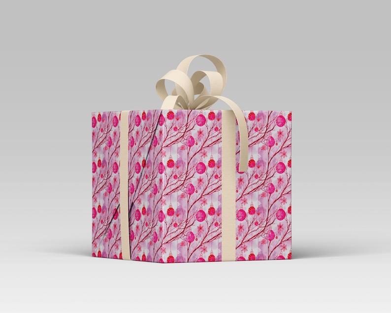 May include: A wrapped gift box with a cream-colored bow. The box is covered in a pink and red pattern of branches, ornaments, and flowers. Cream-colored ribbon wraps around the box. The gift box is on a white surface.