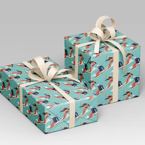 May include: Two gift boxes wrapped in turquoise paper with a repeating pattern of skiers in red, orange, and blue. Each box is tied with a cream-colored ribbon and bow. The boxes are a festive presentation for winter-themed gifts.