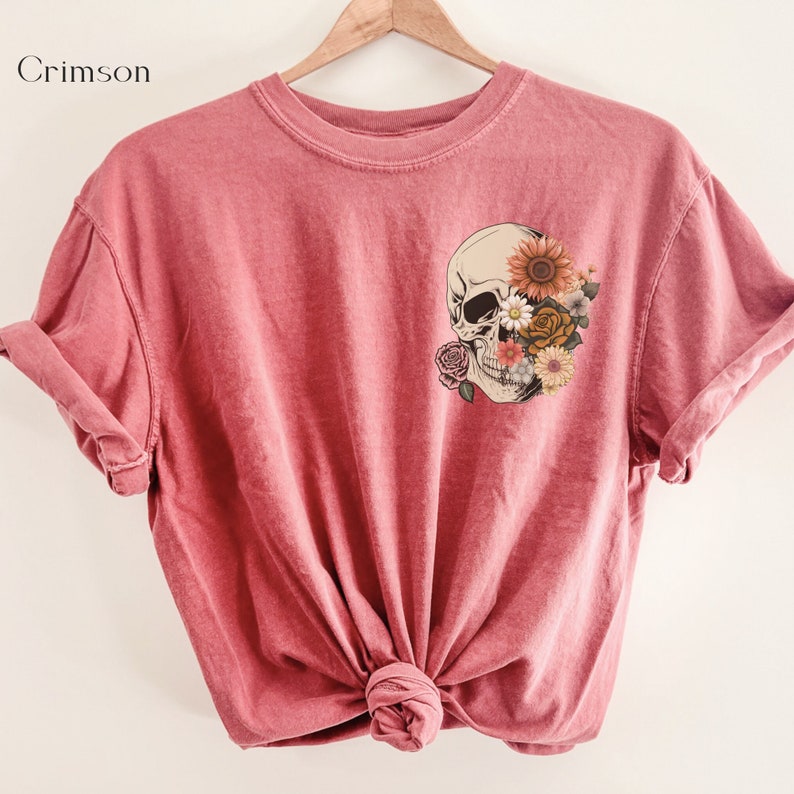May include: A pink t-shirt with a skull graphic. The skull is covered in flowers, including sunflowers, roses, and daisies.