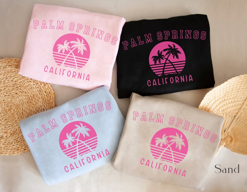 Puede incluir: Cuatro sudaderas de diferentes colores con el texto "Palm Springs California" y un gr&aacute;fico de palmera rosa.