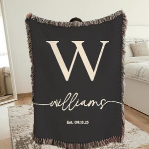 May include: Black woven throw blanket with a large cream-colored letter "W" and the name "williams" in cursive script. The blanket also includes the text "Est. 09.13.25". The edges have a fringed trim.