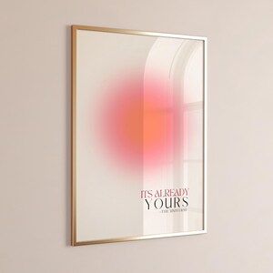 Pode incluir: Um pôster emoldurado em dourado com um fundo degradê rosa e laranja. O texto no pôster diz "It's already yours - The Universe".