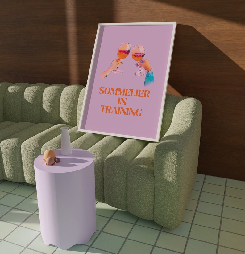 May include: A pink framed print with a graphic of two wine glasses clinking. The text on the print reads "Sommelier in Training".
