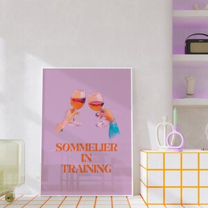 May include: A pink poster with two glasses of red wine clinking together. The text on the poster reads "Sommelier in Training".