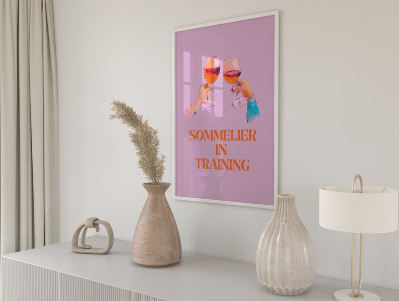May include: A pink poster with a graphic of two hands holding glasses of wine. The text on the poster reads "Sommelier in Training".