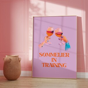 May include: A purple poster with two glasses of red wine clinking together. The text "SOMMELIER IN TRAINING" is printed in orange.
