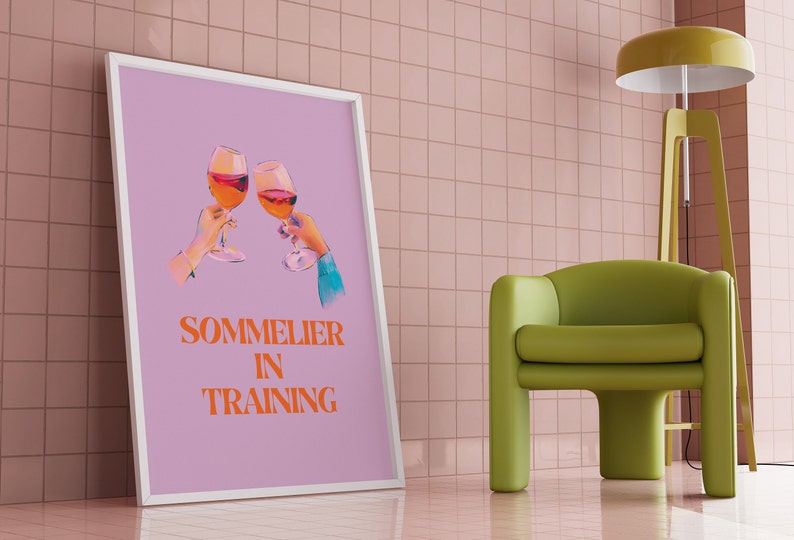 May include: A framed poster with a light purple background featuring two hands holding glasses of wine and the text "SOMMELIER IN TRAINING" in orange.