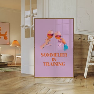 May include: A pink poster with two glasses of wine clinking together. The text "SOMMELIER IN TRAINING" is written in orange letters.