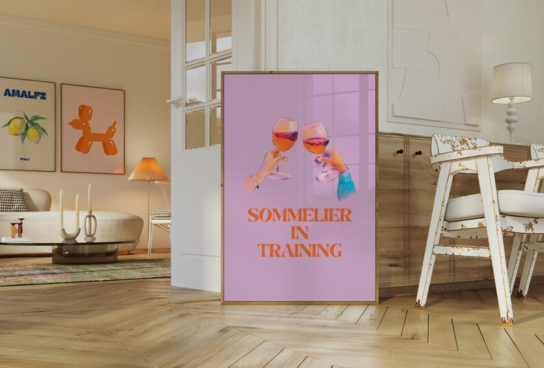 May include: A pink poster with two glasses of wine clinking together. The text "SOMMELIER IN TRAINING" is written in orange letters.