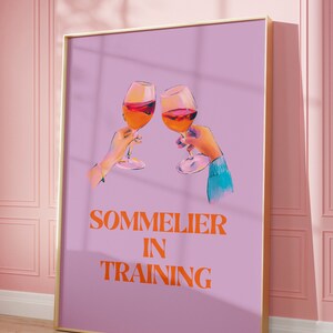 May include: A purple poster with a gold frame featuring two hands holding glasses of wine and the text "SOMMELIER IN TRAINING" in orange.