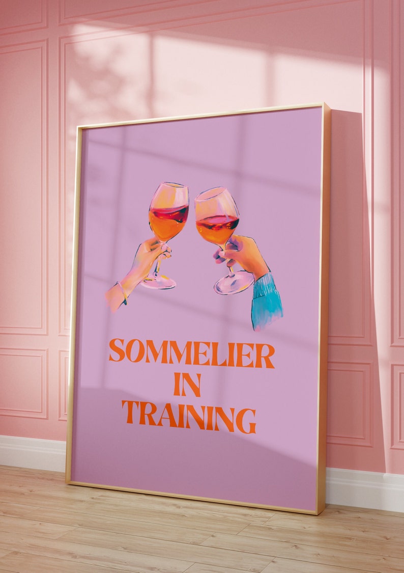 May include: A purple poster with a gold frame featuring two hands holding glasses of wine and the text "SOMMELIER IN TRAINING" in orange.