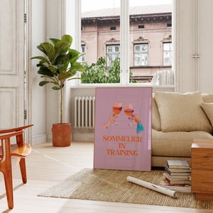 May include: A pink poster with two glasses of wine clinking together. The text on the poster reads "Sommelier in Training".