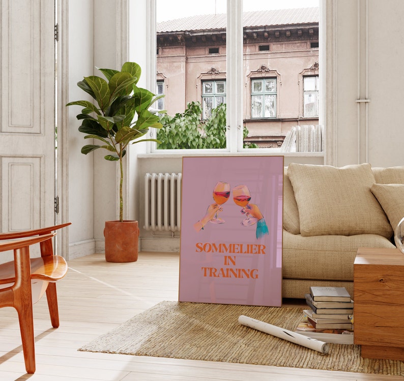 May include: A pink poster with two glasses of wine clinking together. The text on the poster reads "Sommelier in Training".