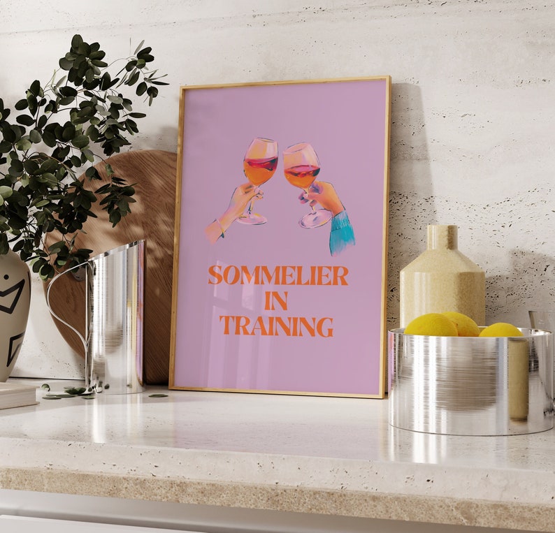 May include: A pink and purple poster with two glasses of red wine clinking together. The text "Sommelier in Training" is written in orange letters.