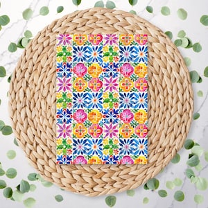 May include: A colorful floral pattern on a rectangular object, featuring vibrant blooms in pink, yellow, and blue. The design is set against a white background and rests on a woven, circular placemat. Eucalyptus leaves are scattered around the placemat.