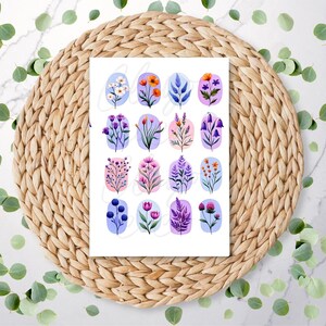 May include: A white sheet of paper featuring watercolor illustrations of various flowers and foliage. Each design is set within a light blue oval, with a mix of colors including pink, purple, orange, and green. The paper rests on a woven, circular placemat.