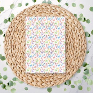 May include: A rectangular sheet of paper featuring a repeating pattern of colourful pencils, butterflies, and small yellow shapes on a white background. The paper is on a woven, circular placemat.