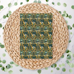 May include: A patterned paper with a repeating design of a woman's face, set against a teal and gold background. The paper is placed on a woven, circular placemat, surrounded by green leaves.