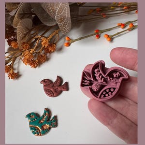 May include: A selection of bird-shaped craft tools and decorative birds. The tools are pink and the birds are brown and teal with copper accents. The tools have intricate designs, and the birds are on a white surface.