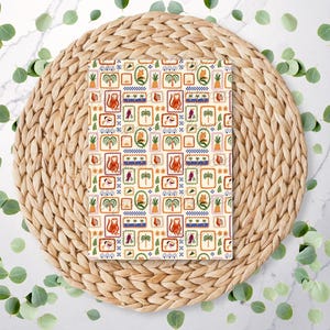 May include: A white fabric with a repeating pattern of colourful squares. Each square features a different design, including palm trees, birds, pineapples, and monkeys. The fabric is displayed on a woven straw placemat.