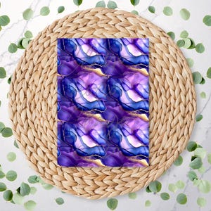 May include: A rectangular pattern featuring an abstract design with shades of purple, blue, and gold. The design is composed of fluid shapes and lines, resembling ink or watercolor art. The pattern is set on a woven, circular placemat.