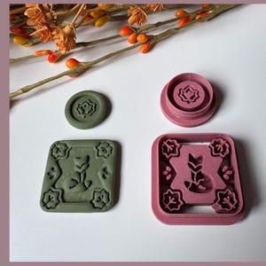 May include: Four cookie cutters in shades of green and pink, featuring floral and fox designs. One is round, two are square, and one is circular. A sprig of orange berries and leaves is in the background.
