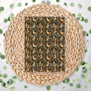 May include: A brown woven placemat with a square piece of fabric on top. The fabric has a repeating pattern of small brown rabbits and flowers on a dark green background.