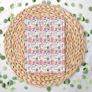 May include: A patterned paper sheet featuring school-themed illustrations. The design includes images of apples, pencils, school buses, and framed pictures, set against a white background. The sheet is placed on a woven, circular placemat, surrounded by green leaves.