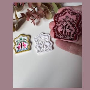 May include: Three decorative stamps featuring a flamingo and palm tree design. One stamp is pink, held in a hand, and the other two are white and yellow. The stamps are in a decorative frame shape.