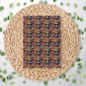 May include: A rectangular fabric with a Japanese-inspired pattern featuring Mount Fuji, cherry blossoms, and traditional buildings. The design is set against a dark background with red, gold, and white accents. The fabric is placed on a woven, circular placemat.