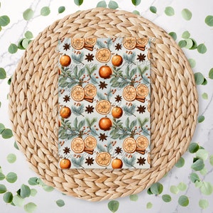 May include: A blue and white patterned wrapping paper with a repeating design of orange slices, cinnamon sticks, and star anise. The paper is on a woven straw placemat.