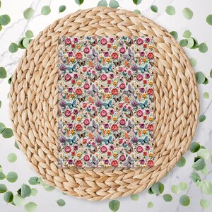 May include: A white fabric with a repeating pattern of colourful butterflies and flowers. The fabric is displayed on a woven straw placemat.