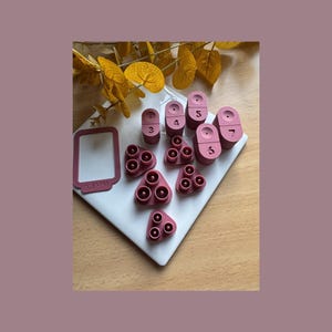 May include: A set of pink silicone molds for making resin jewelry. The molds are shaped like circles, triangles, and squares. The molds are numbered 3, 4, 5, 6, and 7.