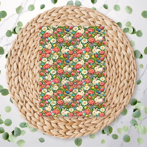 May include: An Easter-themed pattern with white rabbits, red and pink flowers, daisies, and Easter eggs on a dark green background. The design is set on a woven placemat with eucalyptus leaves scattered around.