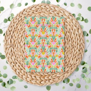 May include: A patterned paper with a repeating design of orange lobsters, pink shells, and green seaweed on a light green background. The paper is set on a woven, circular placemat, surrounded by green leaves.