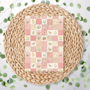 May include: A decorative paper with a patchwork design featuring squares of pink, cream, and beige. The squares display floral patterns, birds, and gingham. The paper is set on a woven, circular placemat, with scattered green leaves.