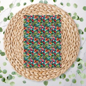 May include: A rectangular sheet with a festive Christmas pattern featuring red and green ornaments, poinsettias, and evergreen branches. The design is set against a dark teal background. The sheet is placed on a woven, circular placemat.