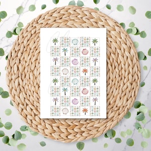 May include: A white gift bag with a repeating pattern of beach-themed icons, including palm trees, seashells, and cocktails. The bag is placed on a woven, circular placemat, with green leaves scattered around the edges.